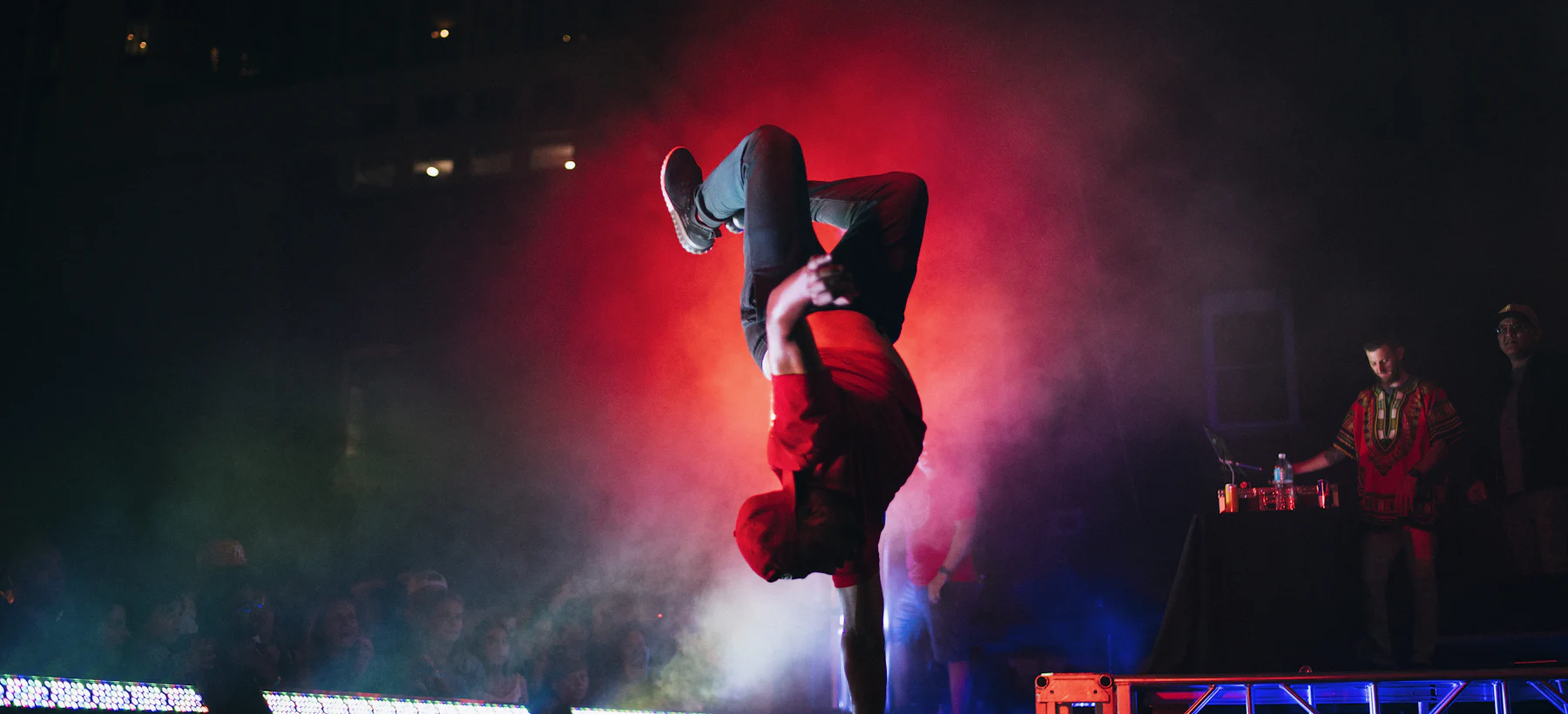 Breakdancer în echilibru pe o mână, pe o scenă cu fum și lumini roșii